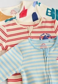 Trois bodies pour bébés : un avec des rayures rouges sur fond crème, un avec des couleurs abstraites et un avec des rayures bleues et crème. En coton doux, avec des encolures rondes.