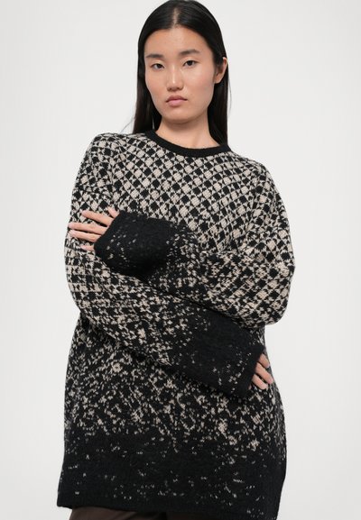 Black and cream knitted sweater featuring a diamond pattern, oversized fit, and extended sleeves with a gradient effect at the hem.