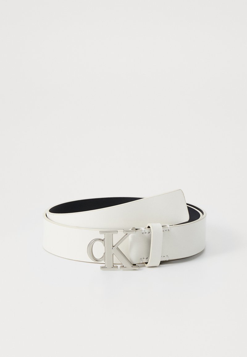 Bela usnjena pas z elegantnim dizajnom, ki ima srebrno CK logo sponko in gladko teksturo. Notranjost je črna, kar nudi kontrast.