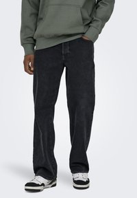 Black denim jeans with a relaxed fit, featuring a subtle texture and standard five-pocket design, paired with white sneakers.