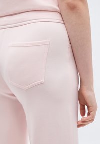 Κοντινό πλάνο στο ισχίο και το χέρι ενός ατόμου που φοράει ανοιχτό ροζ παντελόνια με πίσω τσέπη και ταιριαστό ανοιχτό ροζ τοπ.