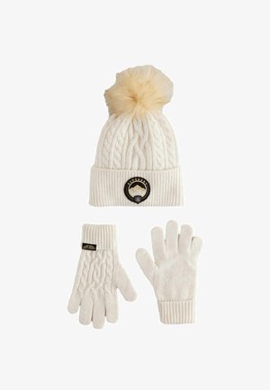 Kremasta pletena zimska postavitev z bolj šalom z pom-ponom, ki ima okroglo Superdry logo in usklajene rokavice, od katerih so ene z detajlom kabelskega pletenja in oznako logotipa.