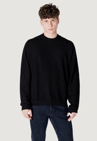 Maglione lavorato a maglia nero con motivo, colletto rotondo e maniche lunghe, caratterizzato da un design testurizzato e polsini e orlo a coste. Abbinato a jeans scuri.