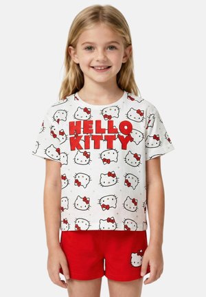 Jeune fille souriante aux longs cheveux blonds portant un t-shirt blanc Hello Kitty et un short rouge avec un visage de Hello Kitty sur la cuisse.