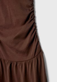 Ruskea kangasmekko, jossa on rypytysdetaljeja sivuilla ja laineikas helma, valmistettu sileästä, joustavasta materiaalista.