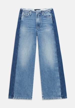 Jean en denim délavé avec un design à jambe large, présentant des panneaux en denim bleu foncé sur les côtés et un ourlet effiloché.