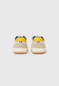 Baskets beige avec des accents jaunes et bleus, finition en daim texturé, rayures subtiles sur les côtés et une semelle en caoutchouc de couleur claire.