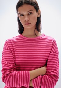 Rózsaszín csíkos hosszú ujjú ing kerek nyakkivágással és széles ujjakkal. Váltakozó világos és sötét rózsaszín vízszintes csíkokkal.