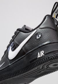 Černá kožená atletická bota s bílými akcenty, gumová podrážka, strukturovaný povrch, výrazné značení "AIR" a nylonová smyčka na tkaničky.