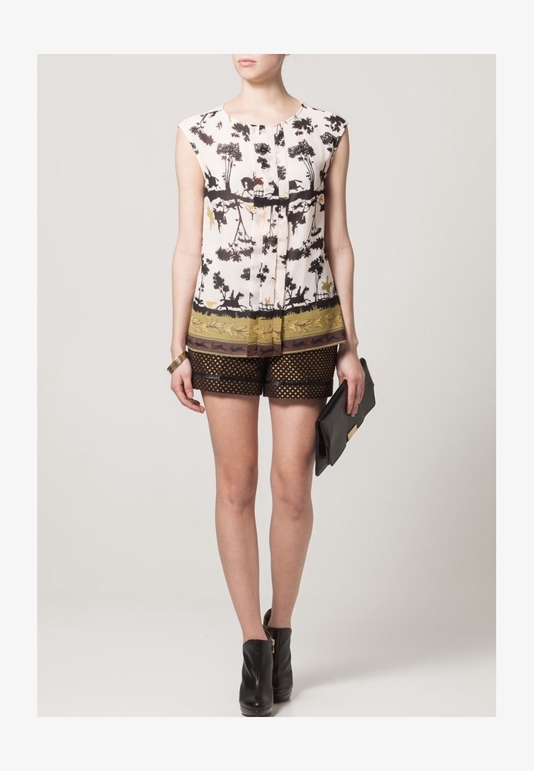Femme portant un haut sans manches à imprimé nature et animaux noir et beige, un short transparent noir à pois, des bottines noires, et tenant une pochette noire.