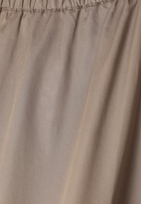 Gonna con elastico beige in vita, tessuto liscio e sottili pieghe verticali.