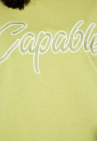 T-shirt verde chiaro con la scritta ricamata "Capable" in bianco, dal design informale e un tessuto morbido e texture.