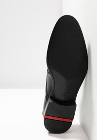 Schwarze Ledersohle mit einer glatten Oberfläche. Verfügt über einen roten Akzent an der Ferse und sichtbare Nähte entlang der Kante für zusätzliche Details.