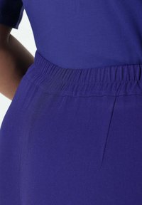 Prenda púrpura con una tela suave y elástica. Presenta una cinturilla elástica y una textura lisa, con un detalle de costura lateral visible.