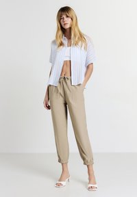 Camicia a maniche corte a righe blu chiaro e bianche con bottoni, top corto bianco, pantaloni beige con coulisse elastica, e sandali bianchi con tacco.