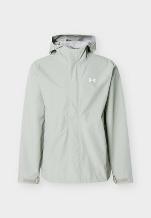 Lysegrå vanntett hettejakke med lange ermer, frontglidelås, borrelåsstropper på ermene og hvit Under Armour-logo på venstre bryst.