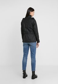 Black textured jacket with a belted waist and high collar, paired with fitted blue jeans and black ankle boots, viewed from the back.