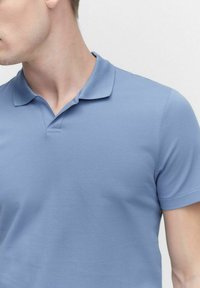 Ljusblå pikétröja i texturerad bomull, med krage och korta ärmar, samt en knappslå under kragen.