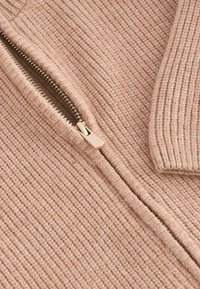 Bežna zip-up jopica z ribasto strukturo, ki ima zlat zadrgo in rahlo zavihan ovratnik. Tkanina izgleda mehko in udobno.