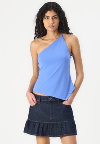 Top azul de un solo hombro en tejido suave, combinado con una falda de mezclilla oscura con dobladillo con volantes y bolsillos frontales.