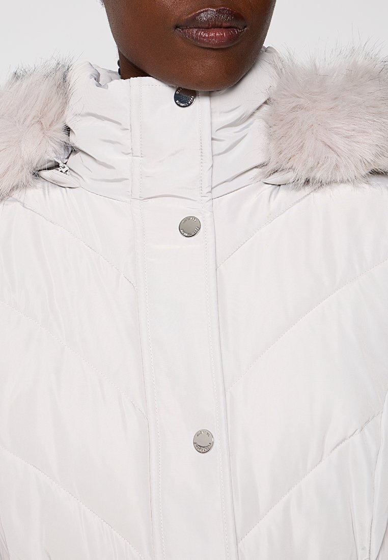 Biała puchowa kurtka z wysokim kołnierzem, srebrnymi zatrzaskami i wykończeniem z futra ekologicznego na kapture. Teksturowany materiał z diagonalnym pikowaniem.