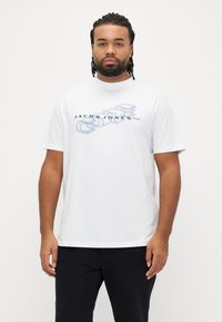 Hvid t-shirt med korte ærmer med et grafisk tryk og teksten "JACK & JONES" i blå. Fremstillet af et glat, letvægtsstof.
