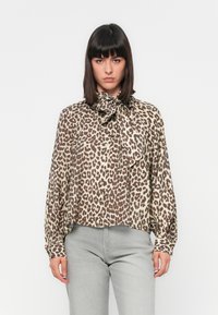 Blusa a stampa leopardata in tessuto leggero, con colletto a fiocco, chiusura frontale con bottoni e maniche lunghe. Palette di colori neutri con accenti marroni.