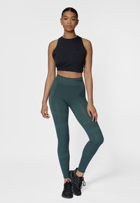 Zwart mouwloos cropped topje met gespikkeld patroon, gecombineerd met donkergroene legging tot op de enkel met gestructureerde panelen en elastische tailleband.