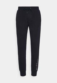 Svarta tapered joggare med dragsko vid midjan och Tommy Hilfiger-logotypen tryckt vertikalt nära vänster vrist.