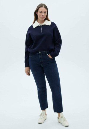 Navy sweater with white collar and zip closure, paired with dark blue straight-leg jeans and white sneakers. Smooth texture throughout.