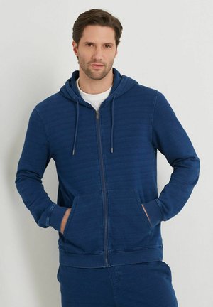 Royal blue zip-up hoodie made of soft fabric, featuring a hood, front pockets, and ribbed cuffs. Light texture with subtle horizontal stripes.