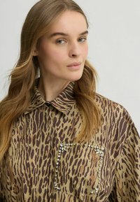 Bruine en beige dierenprint shirt met een kraag, voorzien van een grote zak versierd met rhinestones, gladde stof en een lose fit.
