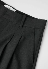 Pantalons en laine gris avec une taille plate, deux plis à l'avant et une texture lisse, comportant une étiquette d'entretien visible à l'intérieur de la taille.