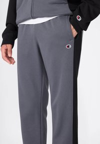 Graue und schwarze Sweatpants mit elastischem Bund, Seitentaschen und einem kleinen Logo. Weiche Textur, gerade Passform und Farbblock-Design.