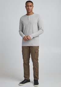 Grå langermet henley-skjorte med tre-knappers placket, kombinert med brune cargo-bukser. Svart sneakers fullfører antrekket, og viser en uformell stil.