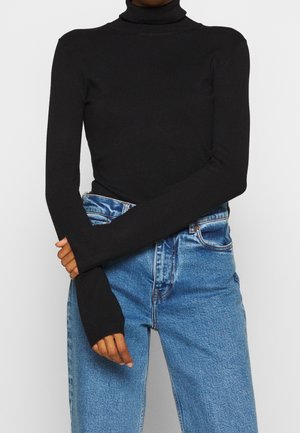 Schwarzes Rollkragenoberteil aus einem dehnbaren, glatten Stoff. Lange Ärmel mit erweitertem Manschettendesign, kombiniert mit hochtaillierten blauen Jeans.