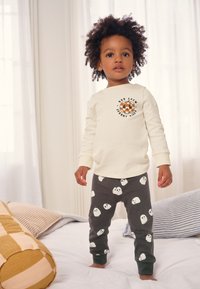 Cremefarbenes Langarmshirt mit Kürbisgrafik, kombiniert mit grauen Hosen mit weißen Geistermustern. Gemütlicher, weicher Stoff und lockere Passform.