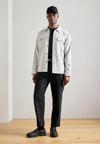 Ανοιχτό γκρι σακάκι με δύο τσέπες στο στήθος, μαύρο μπλουζάκι από κάτω, μαύρο παντελόνι και μαύρα παπούτσια με χοντρή σόλα. Φοράει μαύρο καπέλο.