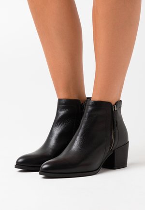 Černé kotníkové boty z kůže s texturovaným povrchem, špičatou špičkou, bočním zipem a blokovým podpatkem, které poskytují elegantní a moderní vzhled.