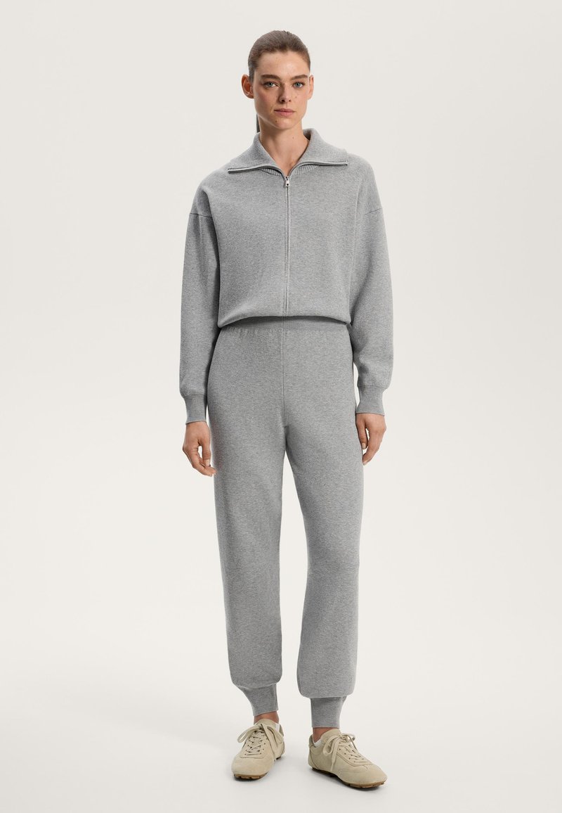 Light gray two-piece outfit made of soft fabric, featuring a zip-up collar and ribbed cuffs, paired with beige sneakers.