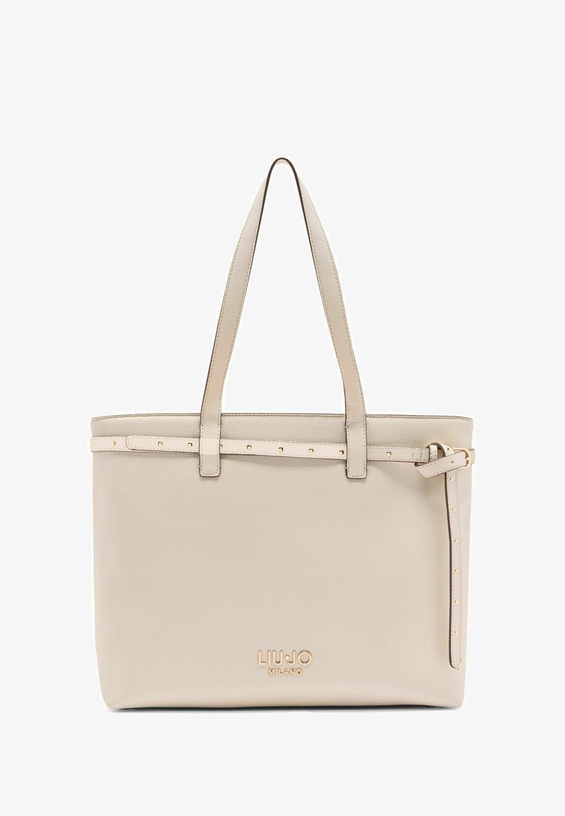 Beige leren tote bag met gouden hardware, voorzien van een studsstrap en een gegraveerd logo aan de onderkant. Open-top ontwerp met twee handvatten.