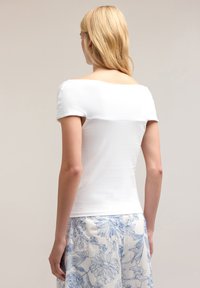 Top blanco de manga corta con escote cuadrado y textura suave, combinado con pantalones de fondo azul con estampado floral.