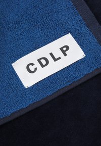 Blå texturerad tyg med en mörk marinblå bottensektion. Har en vit etikett med bokstäverna "CDLP" i svart.