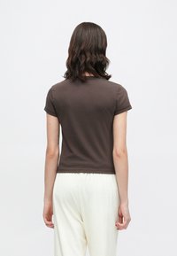 Καφέ κοντομάνικο τοπ με εφαρμοστή σχεδίαση, απαλό ύφασμα και στρογγυλή λαιμόκοψη, συνδυασμένο με ανοιχτόχρωμο, άνετο παντελόνι.