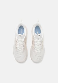 White athletic shoes with a textured mesh upper, flat laces, and soft padding. Features a light blue insole and subtle branding.
