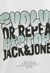 Balta medvilnė marškinėliai su ryškiu, burbulų formos daugiaspalviu tekstu: "EVOLVE OR REPEAT HISTORY JACK & JONES" su papildomu tekstu apačioje.