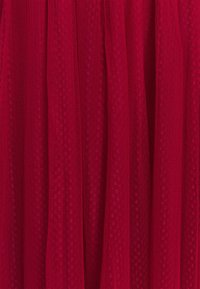 Tela roja con un patrón de puntos abiertos y texturizados; los pliegues caídos crean una apariencia estratificada; material suave y ligero.