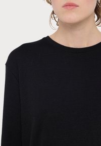 Haut noir à manches longues avec un col rond et un tissu texturé. Présente une coupe décontractée et des détails de couture subtils.