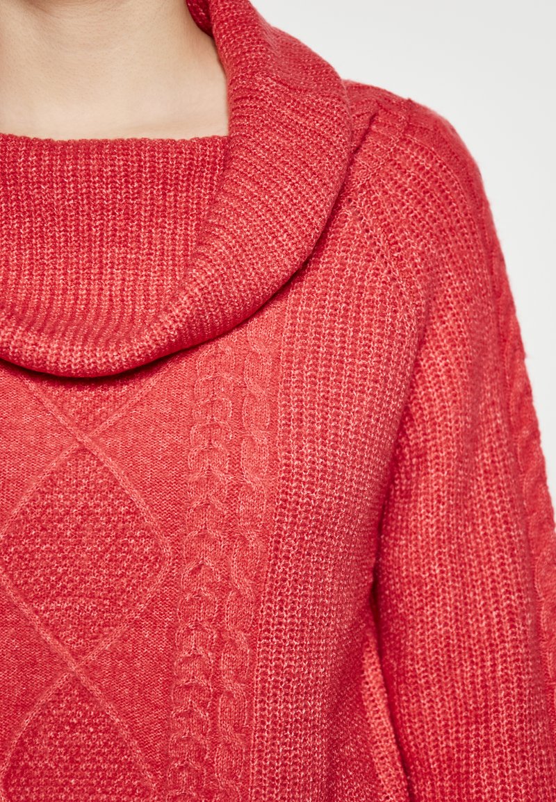 Pulover roșu cu guler în formă de capișon, având un tricotaj texturat, modele în diamant și cablu, și o țesătură caldă și moale. Vedere de aproape a gulerului și părții frontale.