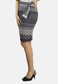 Falda de longitud a la rodilla en color azul marino con estampado de lunares blancos, detalle de lazo en la cintura y textura suave; combinada con zapatos de tacón alto negros.